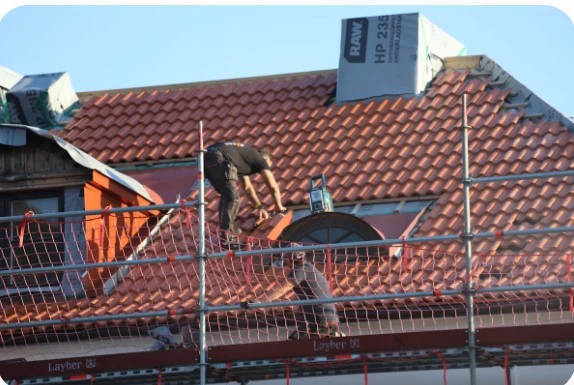 Un ouvrier de Supreme Toiture installe des tuiles en terre cuite rouge sur une toiture en cours de rénovation.